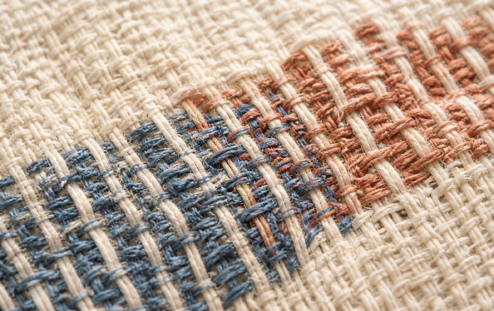 Close-up of a handwoven textile where blue and clay threads are worked into one cloth